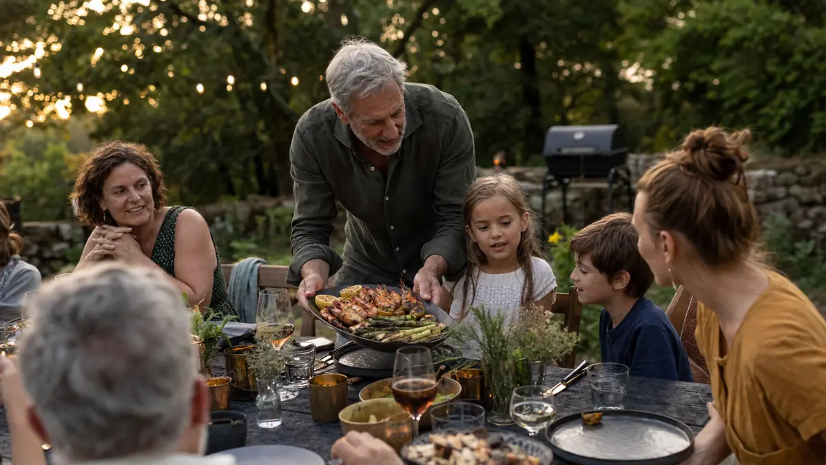 A family gathered around a backyard picnic table eating a platter of grilled vegetables and shrimp