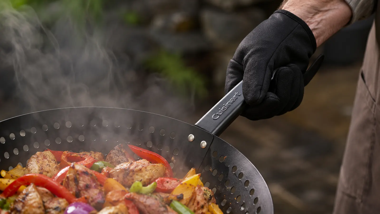 Close-up of a hand holding the Cuisinart Grill Wok handle with a grill glove, testing how hot it gets
