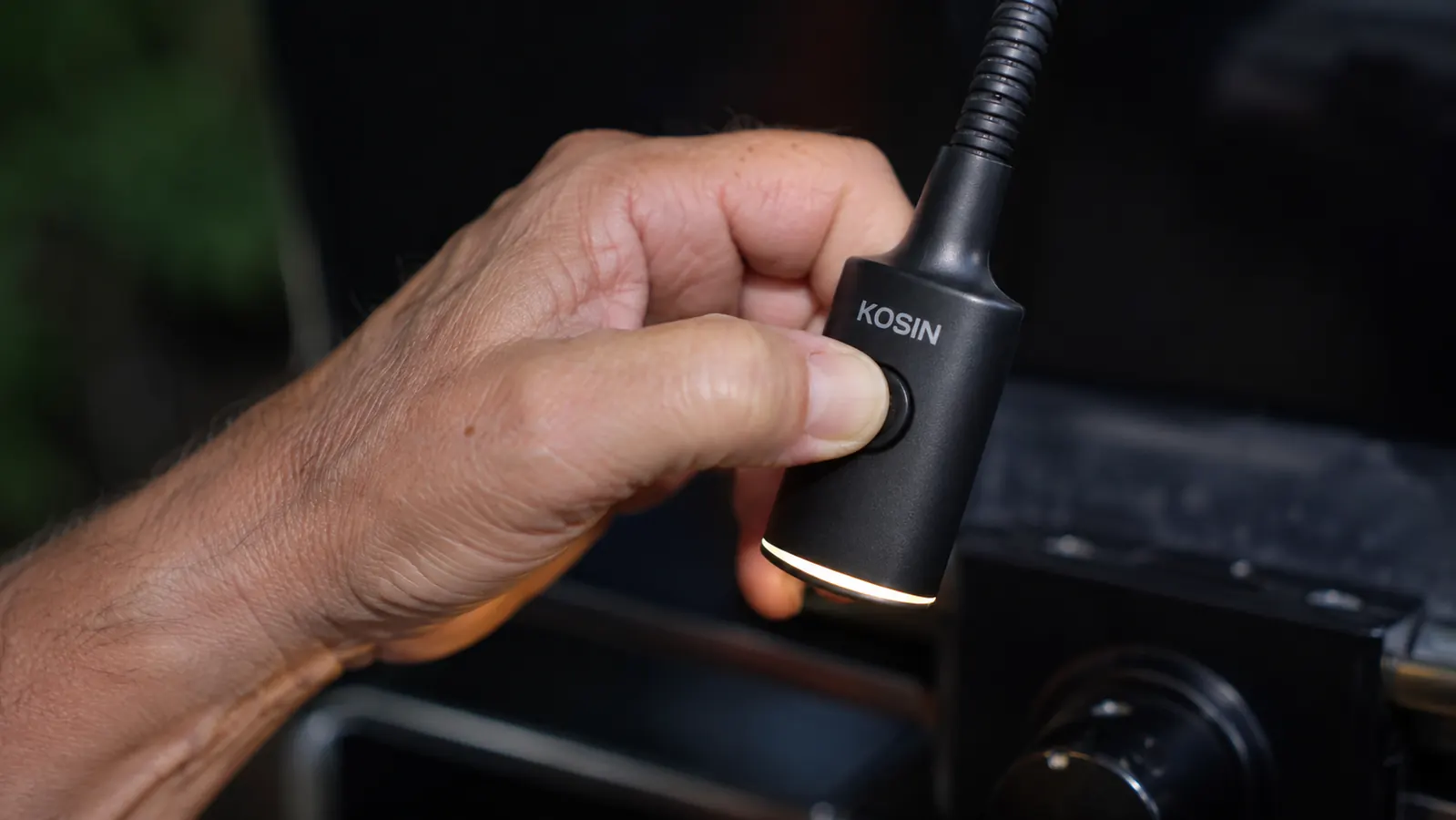 A hand pressing the on/off switch on a clip-on grill light, thumb applying visible pressure