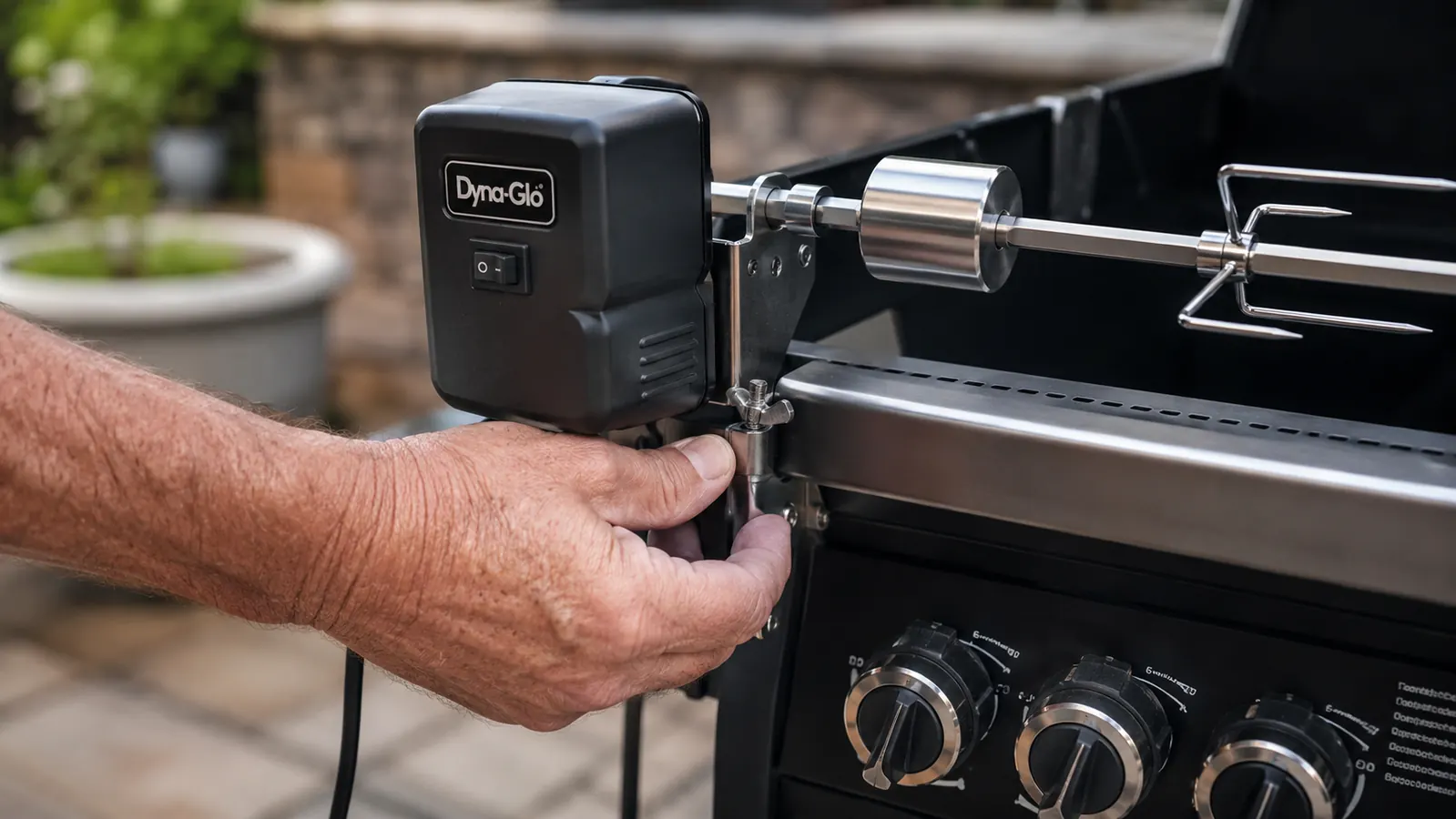Close-up of a hand clamping the Dyna-Glo Universal Rotisserie Kit's motor bracket onto the side of a gas grill