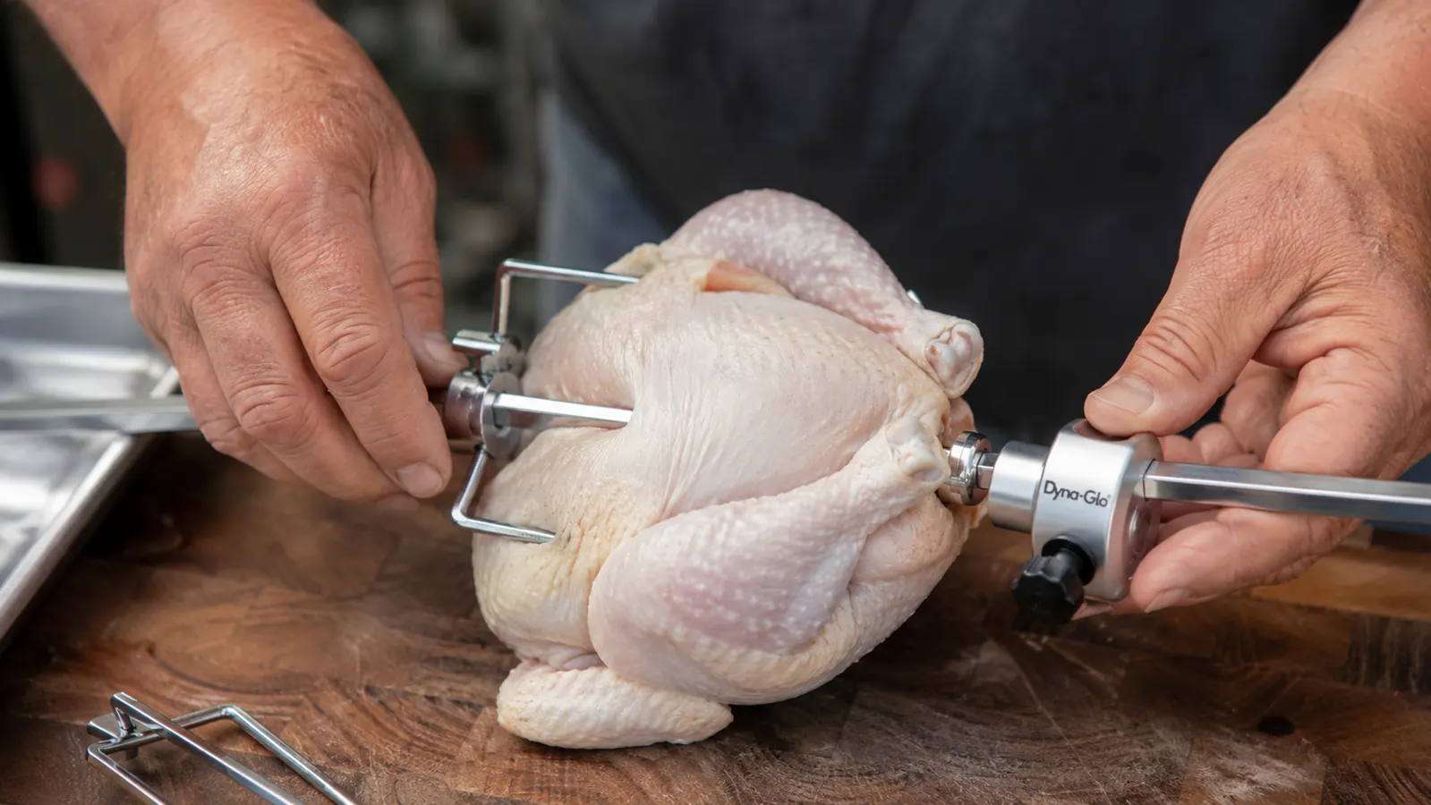 Hand mounting the Dyna-Glo rotisserie forks and counterweight onto a whole chicken before loading it on the grill