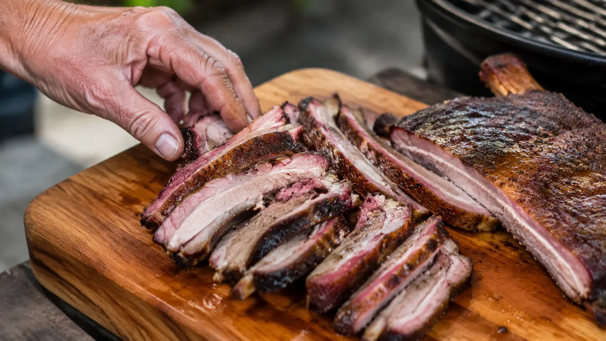 A rack of ribs on a gas grill grate with a visible pink smoke ring along the cut edge