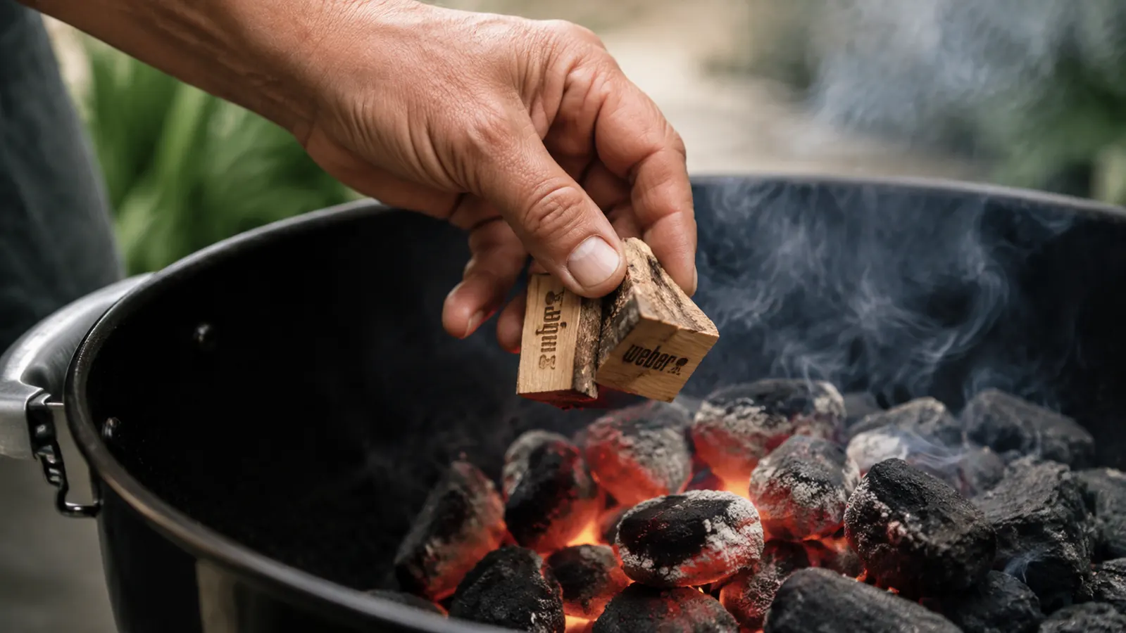 Hand placing Weber hickory wood chunks directly onto glowing charcoal in a kettle grill